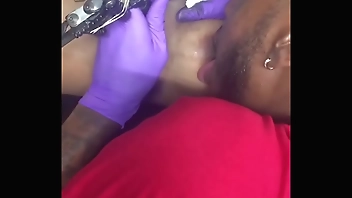 Horny tattoo artist multi-tasking sucking client's nipples